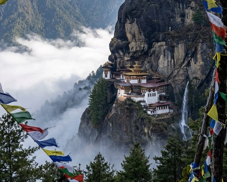 Paro Taktsang, the Tiger's Nest monastery, clinging to a cliff above drifting cloud with prayer flags strung across the foreground